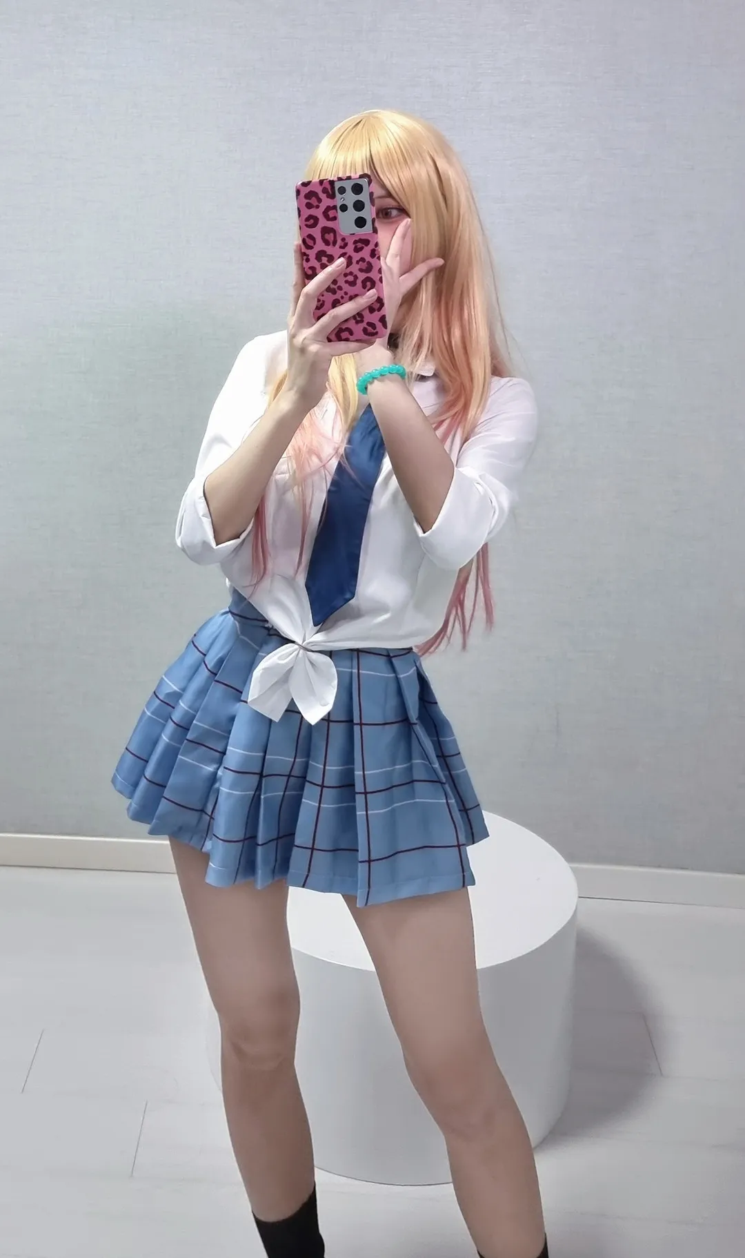 Biya cosplay海外 Biya蓝色格纹裙装照片,站姿位于室内空间中央并手持手机