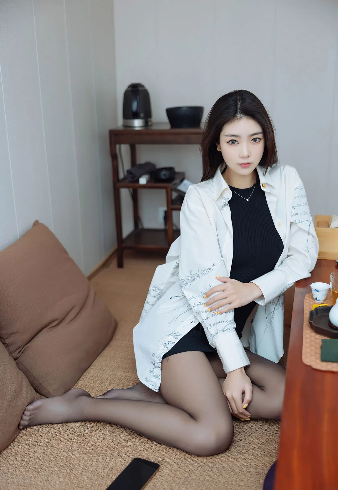 可乐Vicky海外Coser 可乐Vicky白色上衣黑色裙装照片,坐在桌边,室内场景