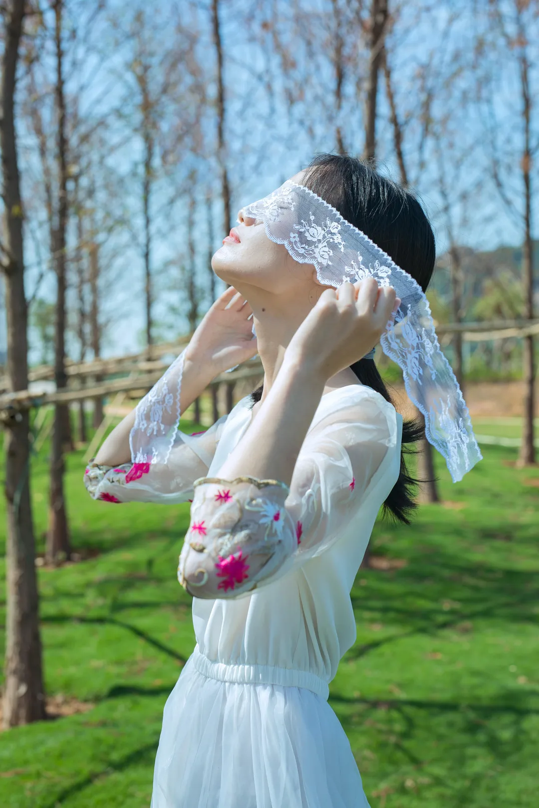 尤蜜丝海外名称 尤蜜丝浅色服装造型照片，人物在户外树木环境中调整头部装饰