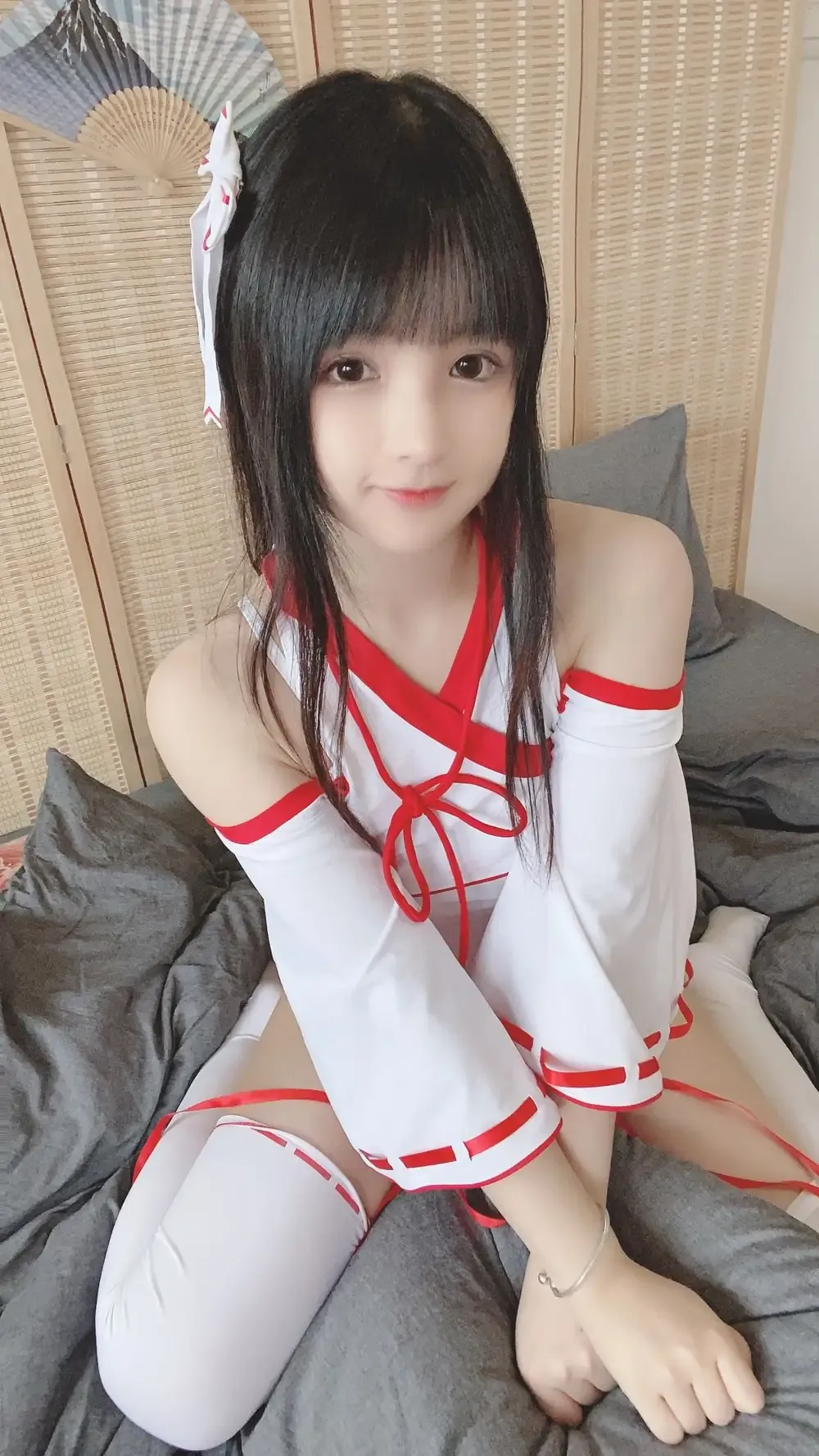 可可小白兔跨语言名称识别与Cosplay作品方向 黑色直发齐刘海人物穿红白配色服装坐在灰色软垫前,背景有浅色屏风与折扇