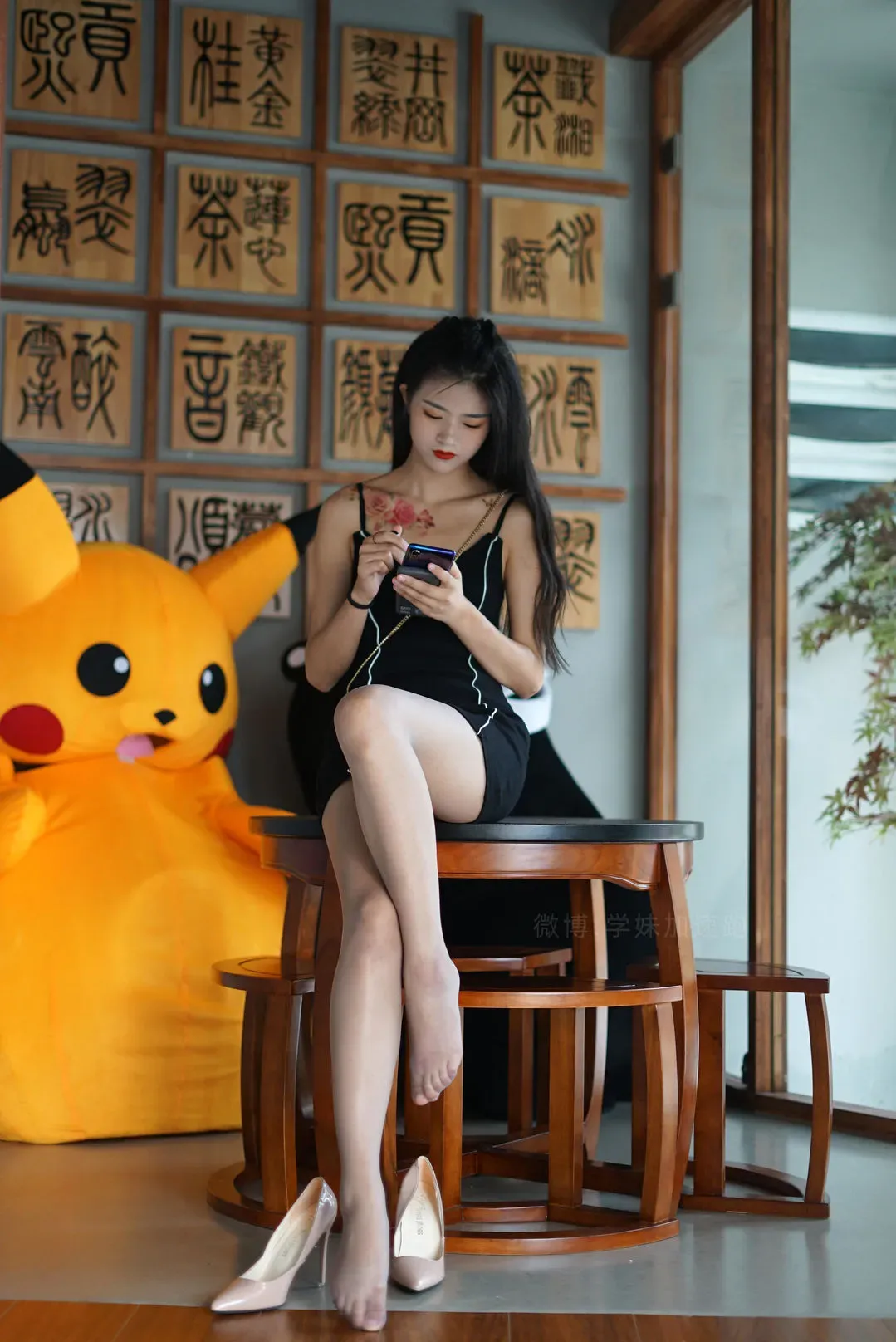 穿着黑色细吊带短裙的模特坐在中式木桌上低头操作手机