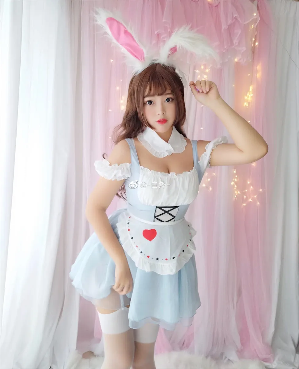 白烨身着浅蓝色女仆装，搭配白色蕾丝围裙与兔耳发箍，站在粉色纱帘背景前