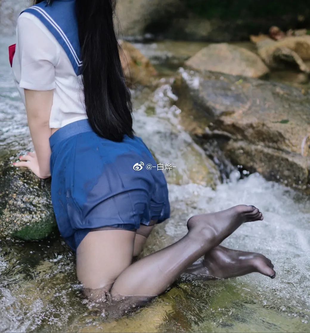 身穿深蓝色水手服与黑色丝袜的身影半跪在户外溪流的浅水石块上