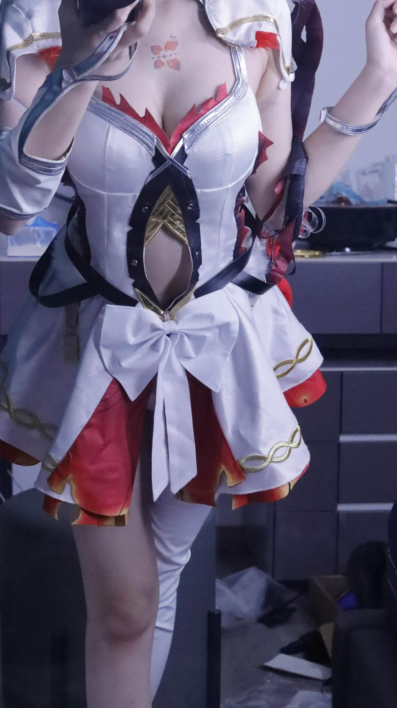 棍之勇者伊蕾娜海外名称识别与Cosplay代表作品 白色与红色搭配的幻想角色服装，衣身带有黑色连接饰件和金色纹样，腰部有白色蝴蝶结，人物站在室内镜面前。
