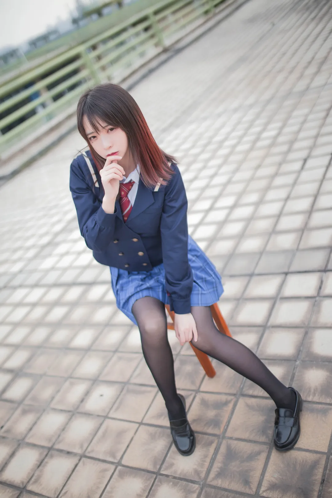 身穿深蓝色西装外套与百褶裙的Cosplay创作者坐在户外石凳上