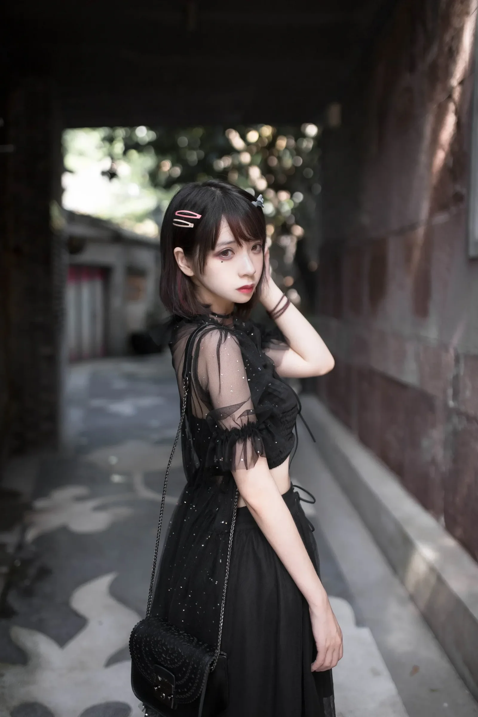 身着黑色透视纱裙的Cosplay创作者侧身站在昏暗过道中