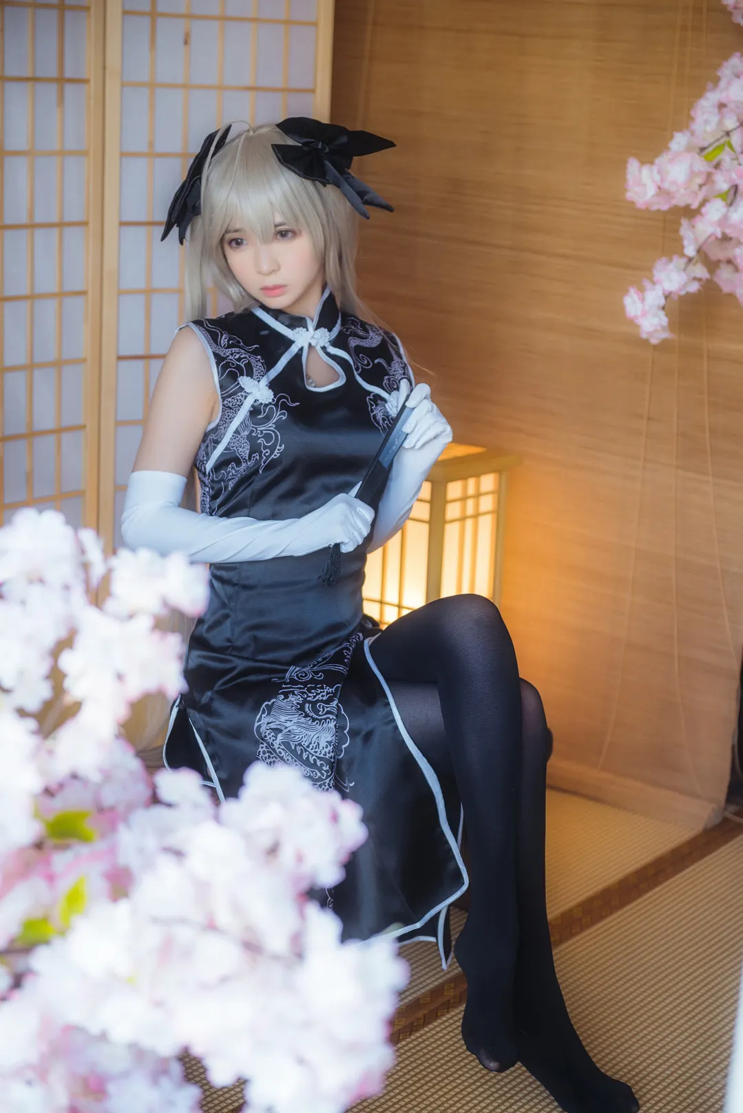 身穿黑底银纹改良旗袍与白手套的Cosplay创作者坐在木制屏风前
